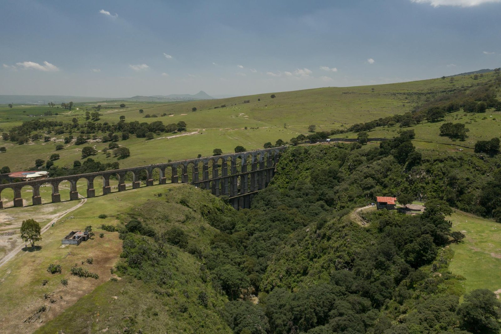 Drone shot capturing the scenic Arcos del Sitio aqueduct amidst lush greenery in Mexico.