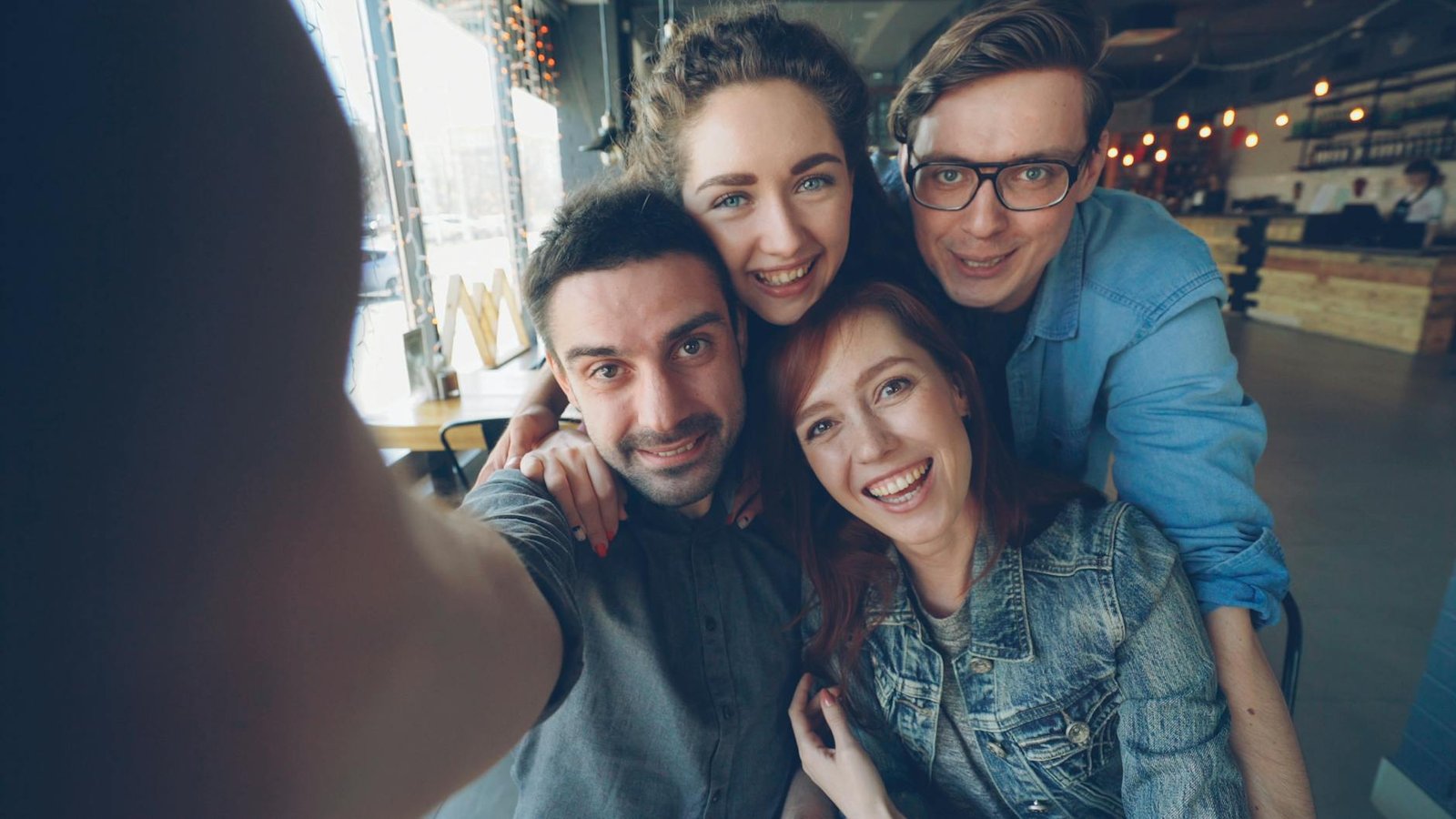 Four friends enjoying a fun moment with a selfie in a lively cafe setting.