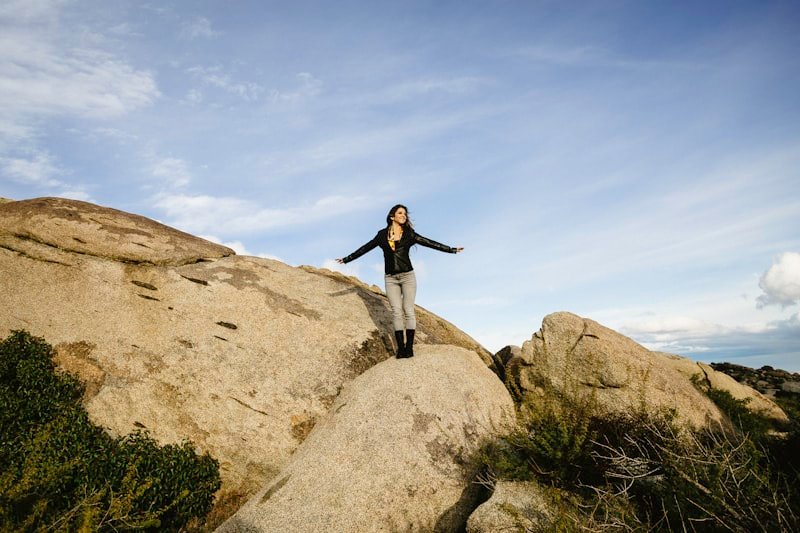 woman in black long sleeve shirt and blue denim jeans standing on brown rock formation during
