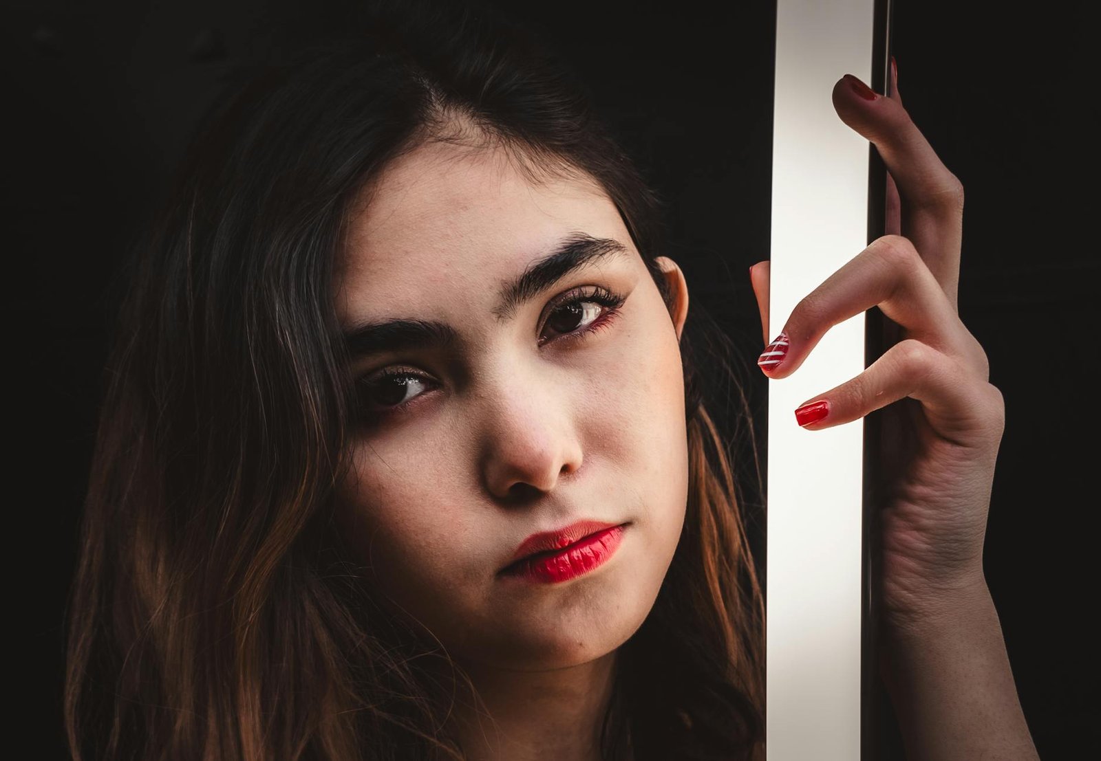 Close-up portrait of a woman with red lips holding a light source, displaying moody ambiance.