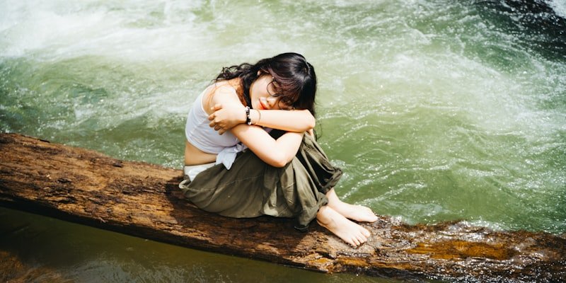 Young woman sitting on a log by a river.
