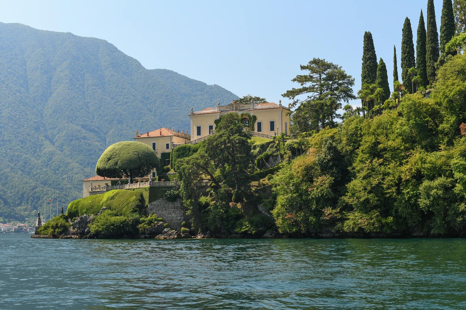 Picturesque villa surrounded by lush greenery on Lake Como, Italy, under a clear blue sky.