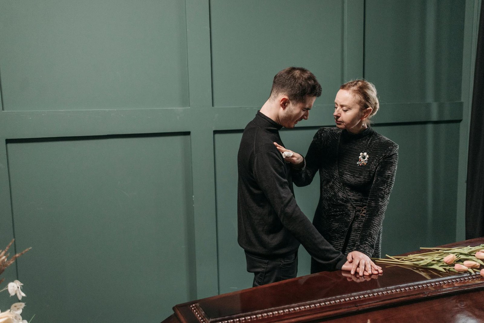 A grieving man and woman comfort each other at a funeral, expressing sorrow and loss.