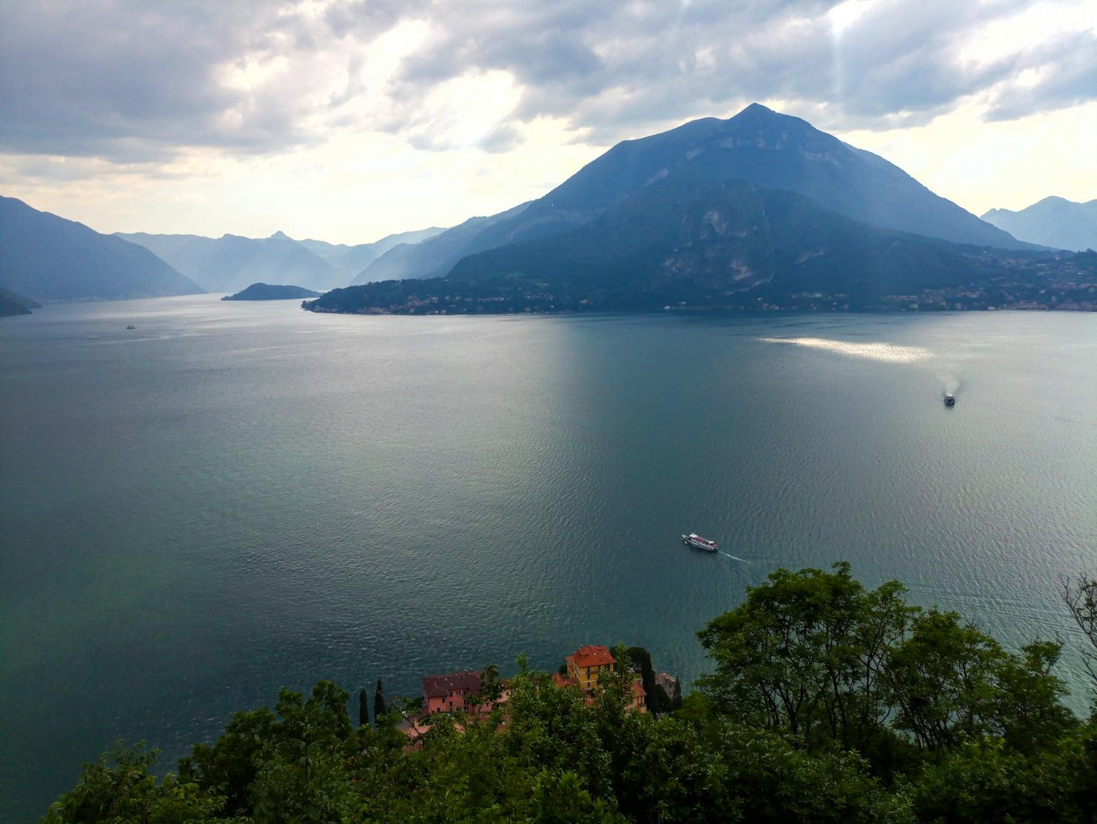 A serene view of Lake Como in Italy with mountains and boats under cloudy skies.