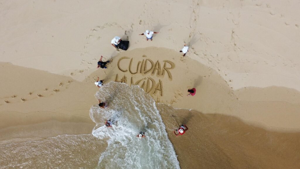 Drone photo of a beach cleanup group in Oaxaca with 'Cuidar la Vida' in sand.