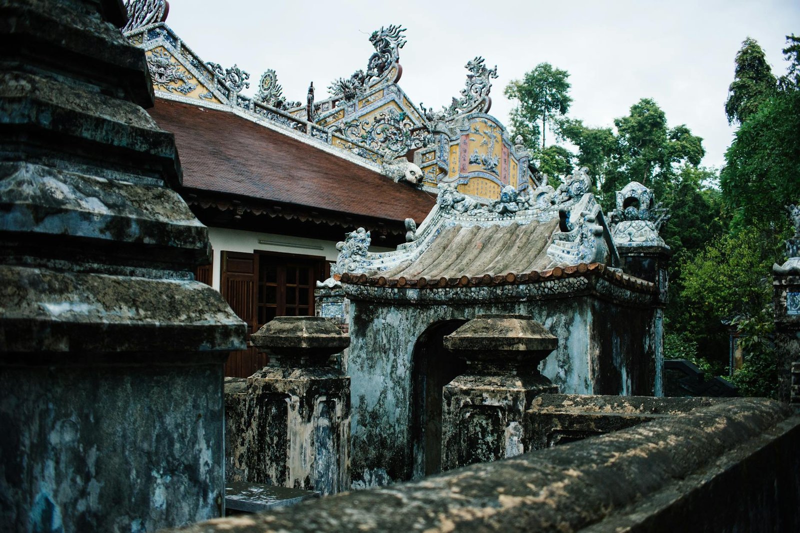 Explore the intricate architecture of an ancient Buddhist temple in Hue, Vietnam, surrounded by lush greenery.