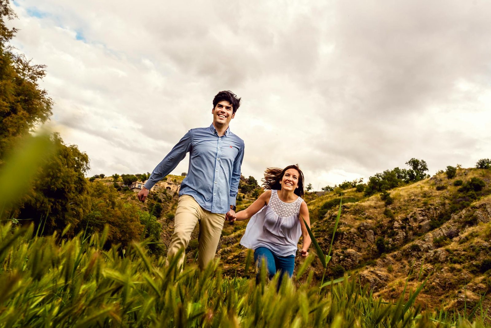Happy couple holding hands and running through Toledo countryside, enjoying summer freedom.