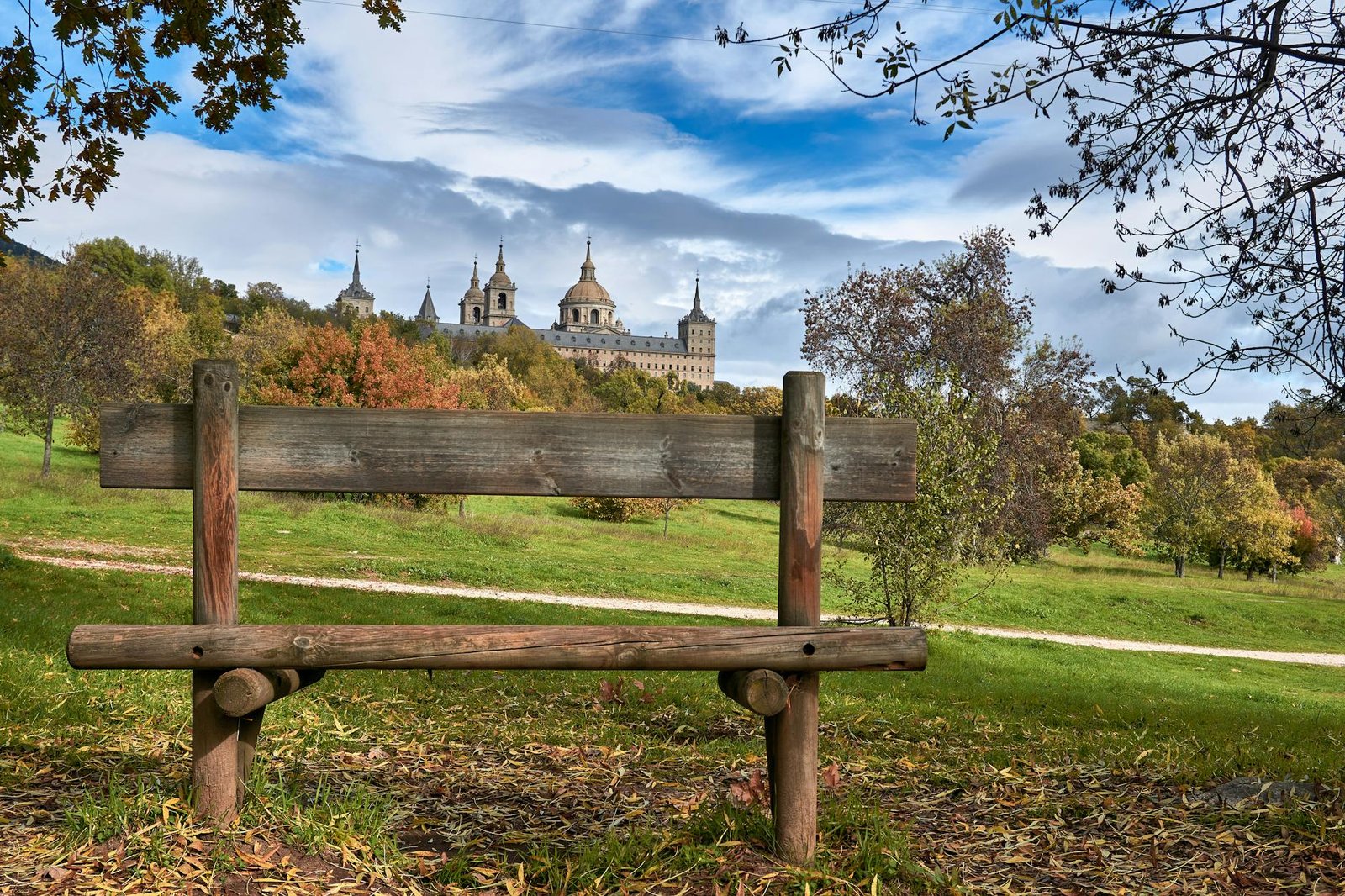 A tranquil scene showcasing El Escorial monastery with a rustic wooden bench in the foreground.