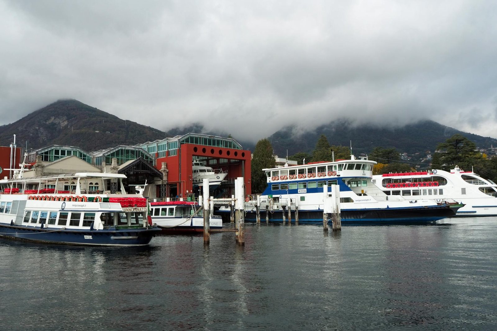 Serene scene of ferries docked at Como's port with mountains and clouds in the backdrop.
