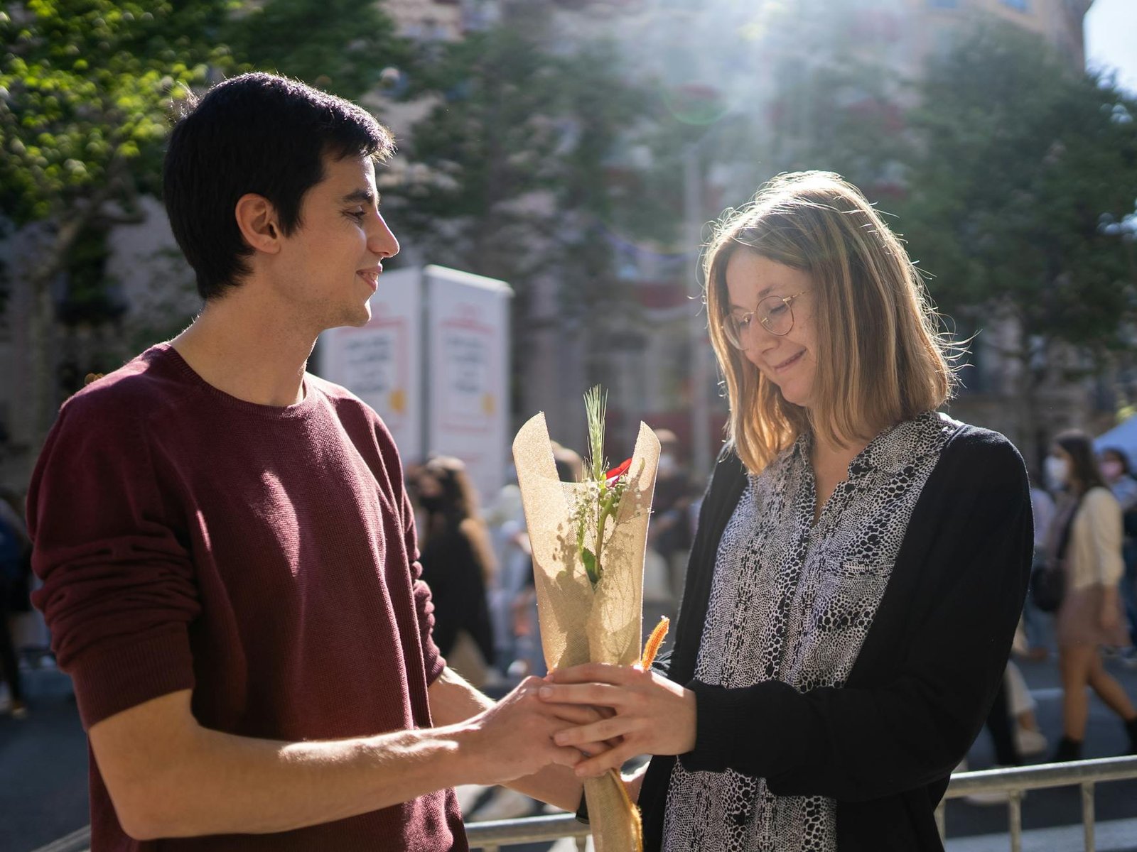 A young couple exchanging flowers outdoors on a sunny day, symbolizing love and affection.