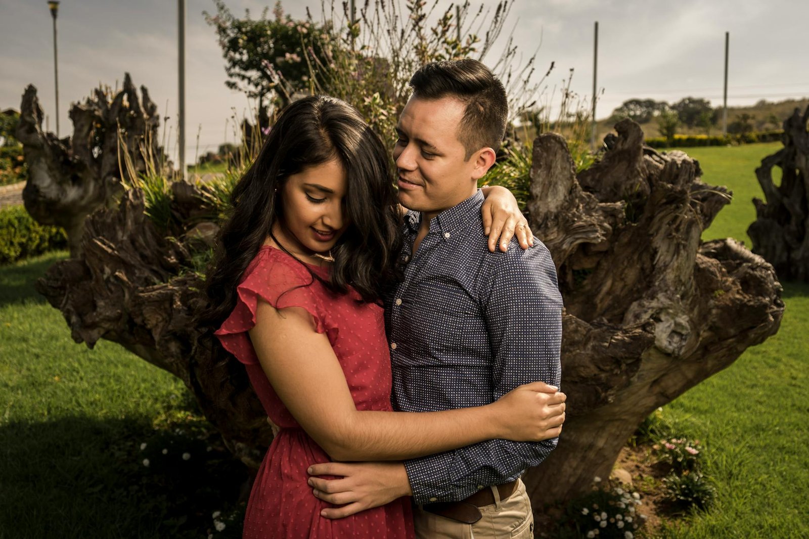 A loving couple embraces in a sunny outdoor setting surrounded by nature.
