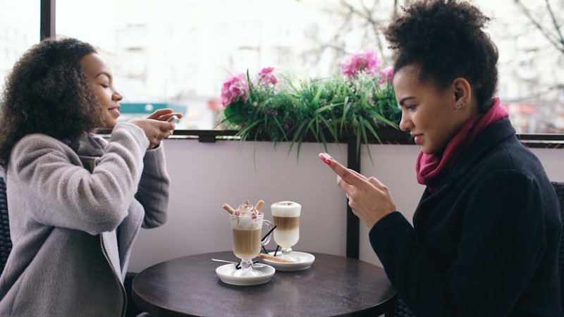 Two women taking photos of coffee at cafe.