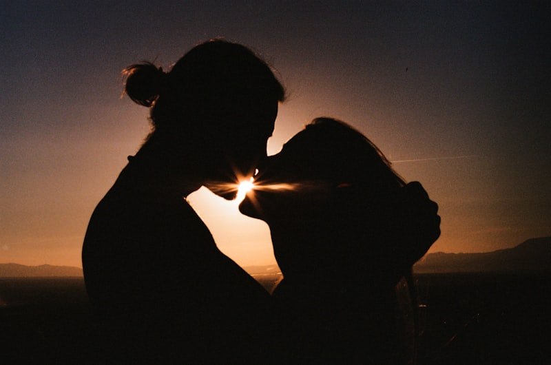 a man and a woman kissing in front of a sunset