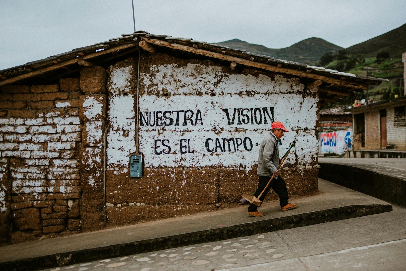 Street sweeper walking past a mural in Cajamarca, Peru, showcasing urban life and local culture.