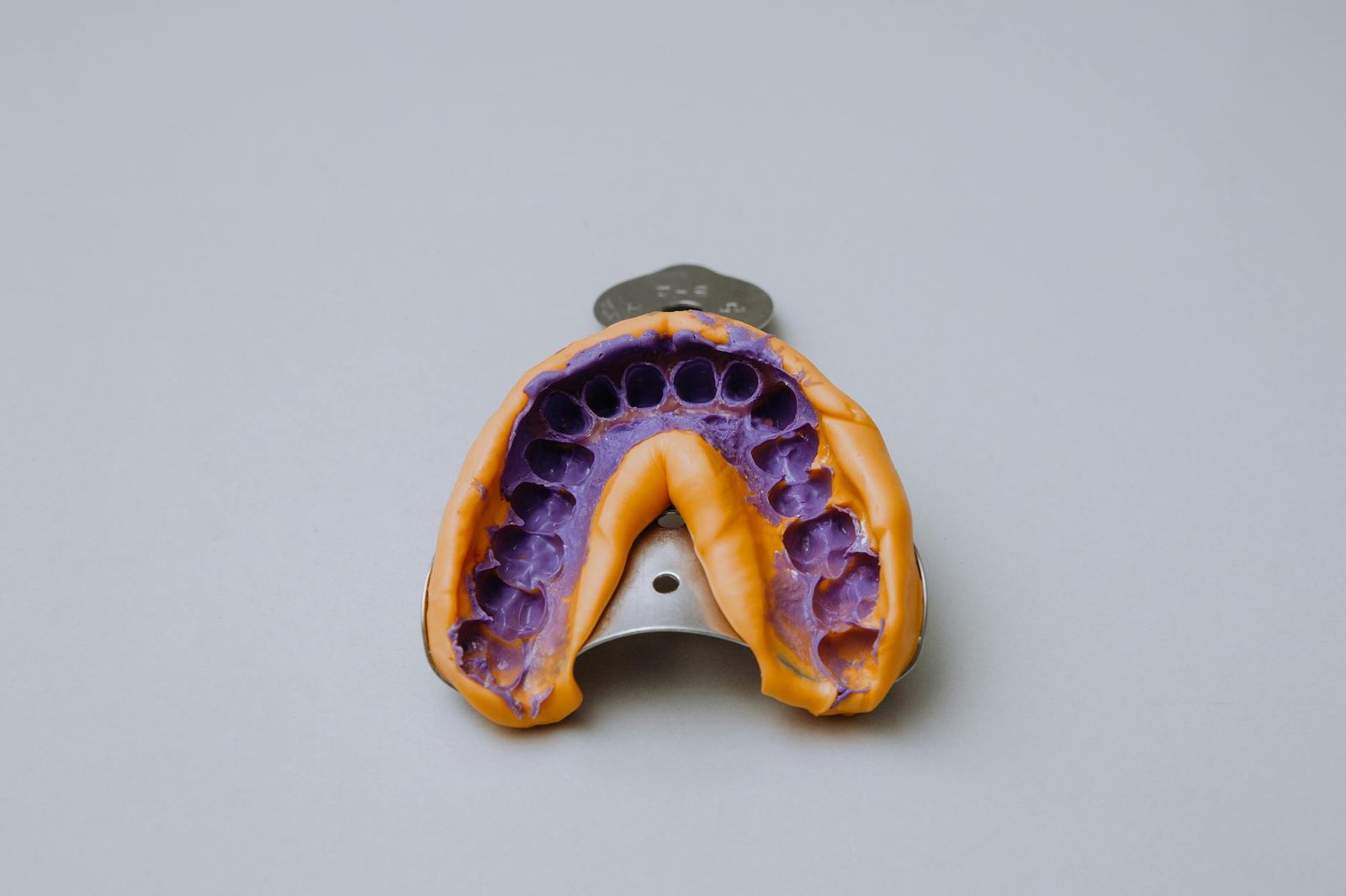 Dental impression tray with purple material on a gray backdrop.