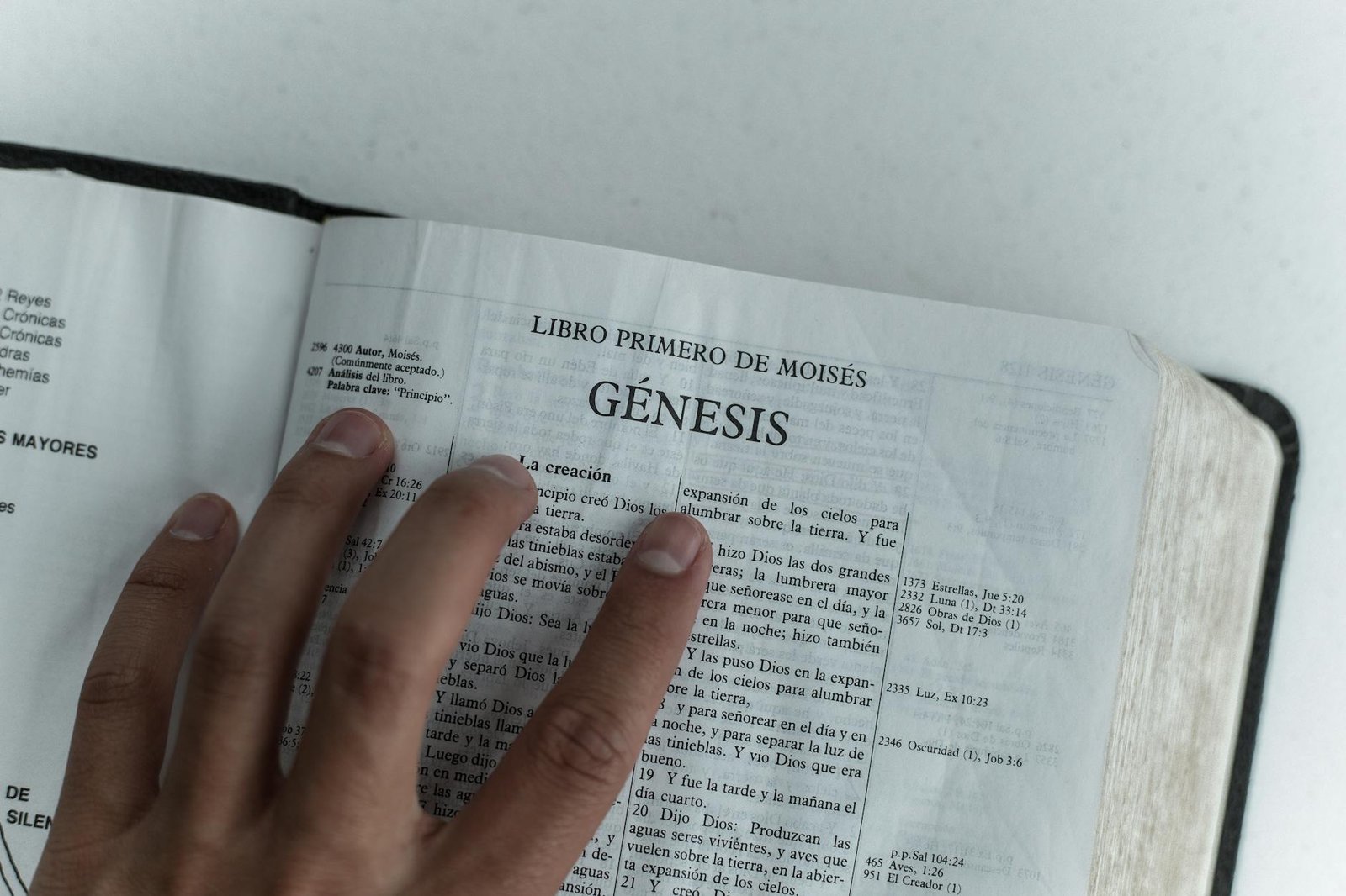 Close view of Genesis chapter in Spanish Bible, hand touching page.