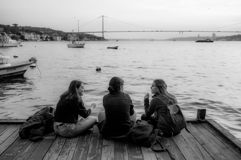A group of people sitting on a dock next to a body of water